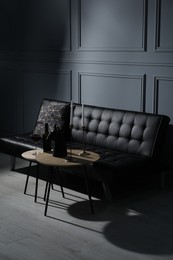 Photo of Elegant leather sofa and candlesticks on coffee table near light grey wall. Interior design