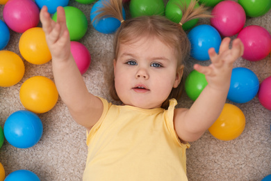 Photo of Cute little child playing with balls on floor, top view