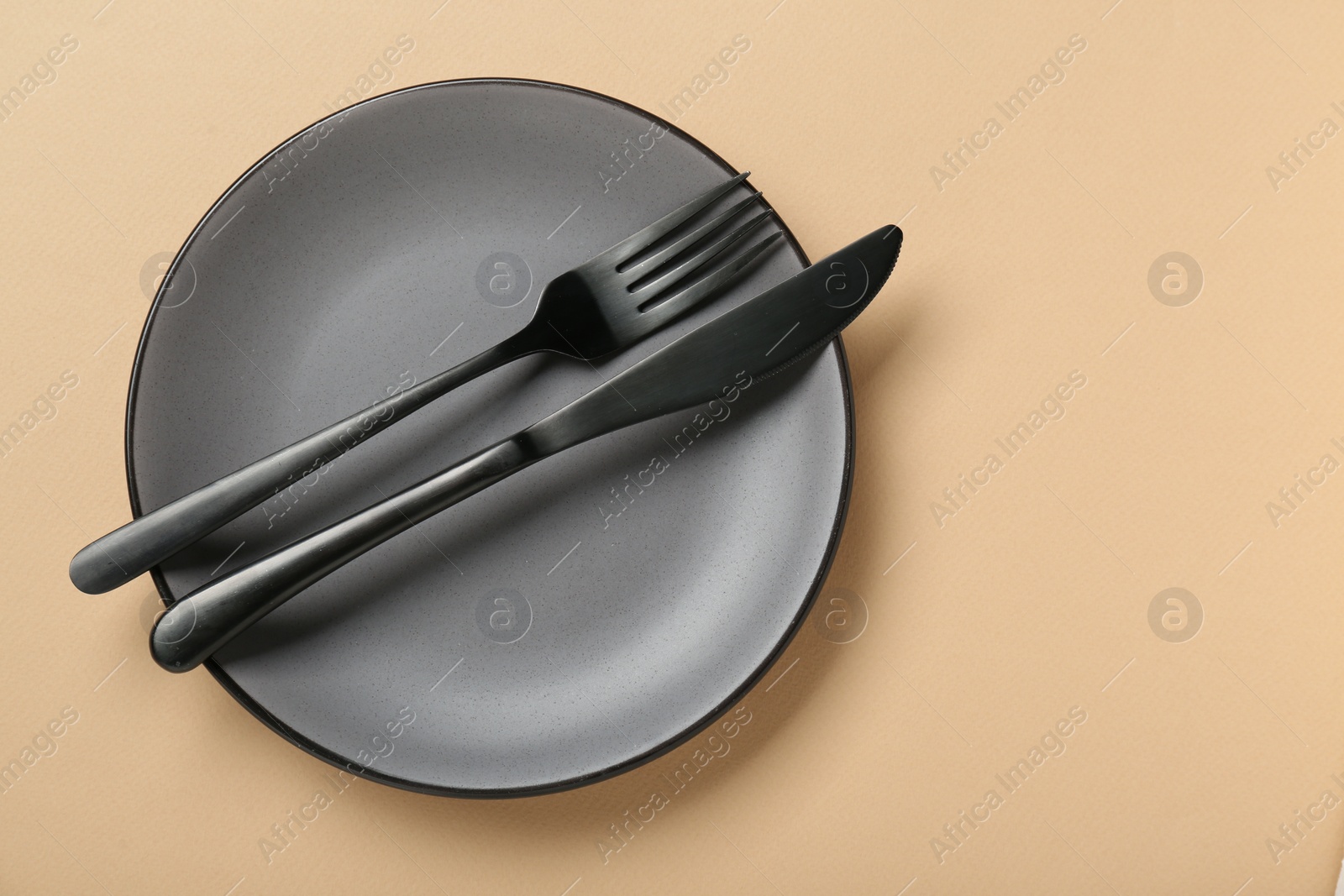 Photo of Grey ceramic plate with cutlery on pale orange background, top view. Space for text