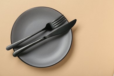 Photo of Grey ceramic plate with cutlery on pale orange background, top view. Space for text