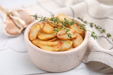 Photo of Fried garlic cloves and thyme in bowl on white table, closeup