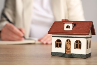 Photo of Mortgage concept. Woman writing at wooden table, focus on house model. Space for text