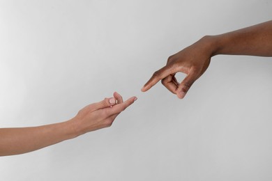 Photo of Woman and African American man touching fingers on light grey background, closeup