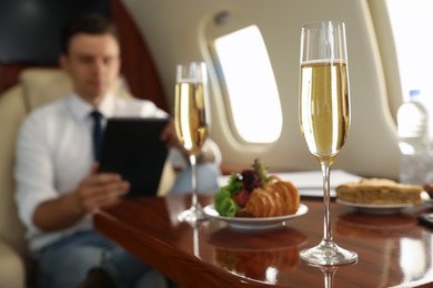 Photo of Businessman working at table in airplane during flight, focus on glass of champagne