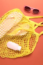Photo of String bag, sunglasses, cosmetic product and slippers on coral background, top view