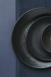 Photo of Stylish ceramic plates, bowl and napkin on dark blue background, top view