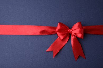 Photo of Red satin ribbon with bow on blue background, top view