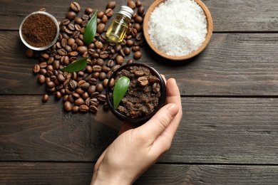 Photo of Woman holding jar of coffee scrub on wooden background