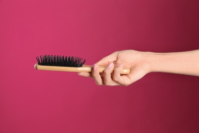 Photo of Woman holding wooden hair brush against crimson background, closeup