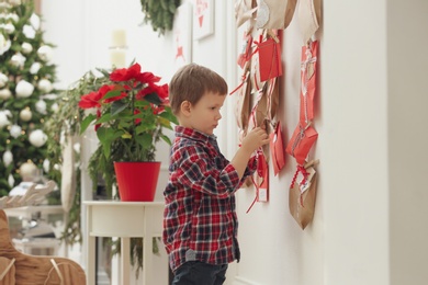 Photo of Cute little boy taking gift from Advent calendar at home. Christmas tradition