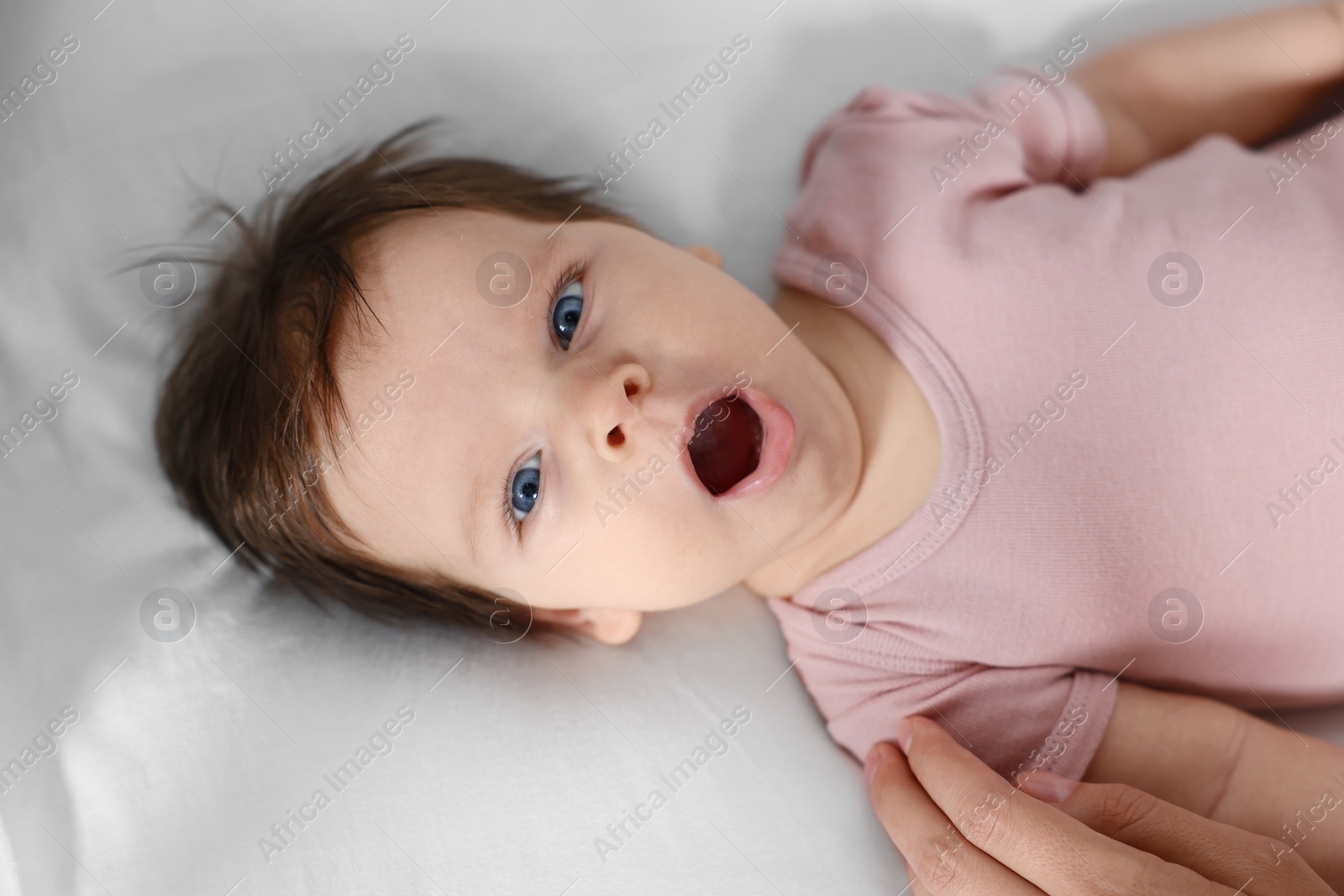 Photo of Cute baby in pink body yawning on bed, closeup