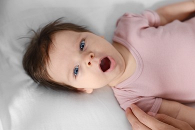 Photo of Cute baby in pink body yawning on bed, closeup
