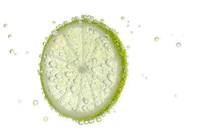 Photo of Fresh lime slice in sparkling water on white background