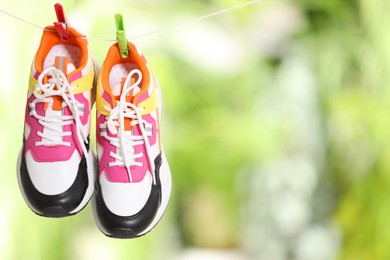 Photo of Stylish sneakers drying on washing line against blurred background, space for text