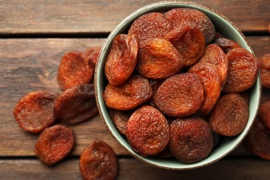 Photo of Tasty apricots with bowl on wooden table, flat lay. Dried fruits