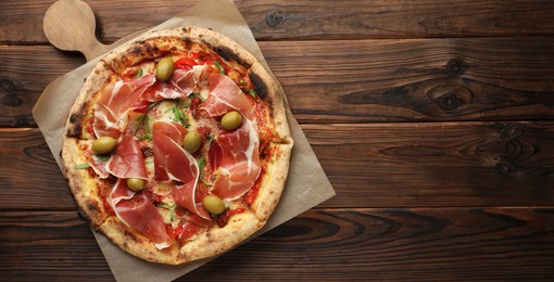 Photo of Tasty pizza with cured ham, olives and sun-dried tomato on wooden table, top view. Space for text