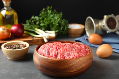 Photo of Raw ground meat in bowl and different products on grey table