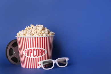 Photo of Delicious popcorn, 3D glasses and movie reel on blue background. Space for text