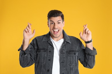 Photo of Man with crossed fingers on yellow background. Superstition concept