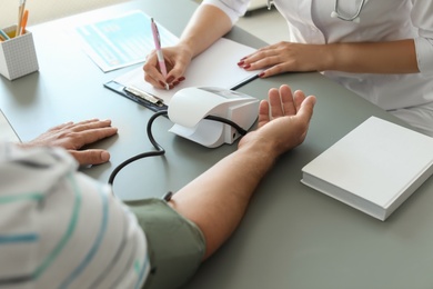 Photo of Doctor checking patient's blood pressure at table in office