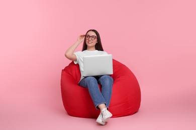Photo of Smiling young woman with laptop sitting on beanbag chair against pink background
