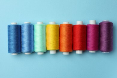 Photo of Set of different colorful sewing threads on light blue background, flat lay