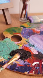 Photo of Artist's palette with mixed bright paints and brush on wooden table