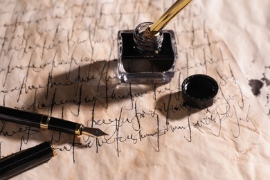 Photo of Open inkwell and fountain pens on vintage parchment with text, closeup