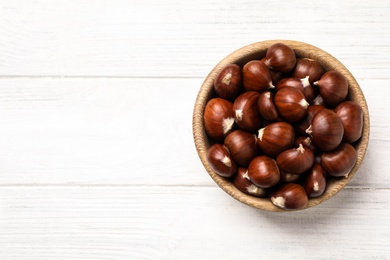 Photo of Fresh sweet edible chestnuts on white wooden table, top view. Space for text