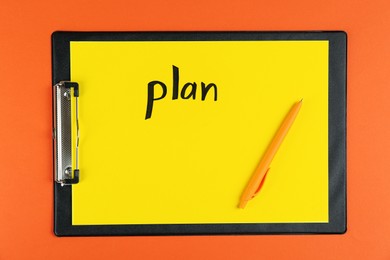 Photo of Clipboard with word Plan and pen on orange background, top view