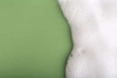 Photo of White fluffy foam on green background, top view. Space for text