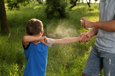 Photo of Man applying insect repellent on his son's arm in park, closeup. Tick bites prevention
