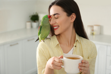 Photo of Young woman with Alexandrine parakeet indoors. Cute pet