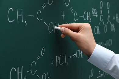 Photo of Teacher writing chemical formulas with chalk on green chalkboard, closeup
