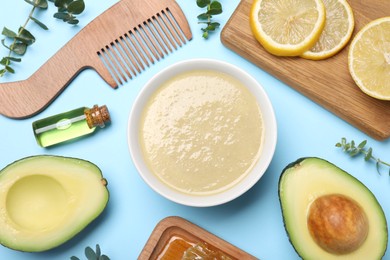 Photo of Homemade hair mask in bowl, fresh ingredients and bamboo comb on light blue background, flat lay