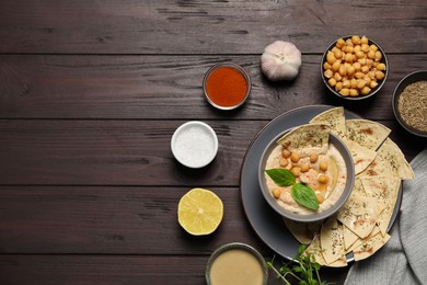 Photo of Delicious creamy hummus with chips and different ingredients on wooden table, flat lay. Space for text