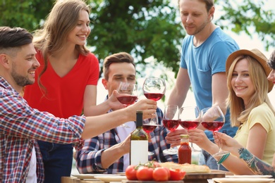 Photo of Young people with glasses of wine at table outdoors. Summer barbecue