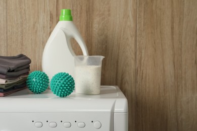 Photo of Dryer balls, stacked clean clothes and detergents on washing machine. Space for text