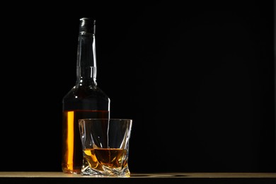 Photo of Whiskey in glass and bottle on table against black background, space for text