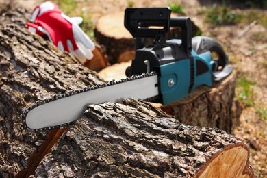 Photo of Modern electric saw and wooden log outdoors