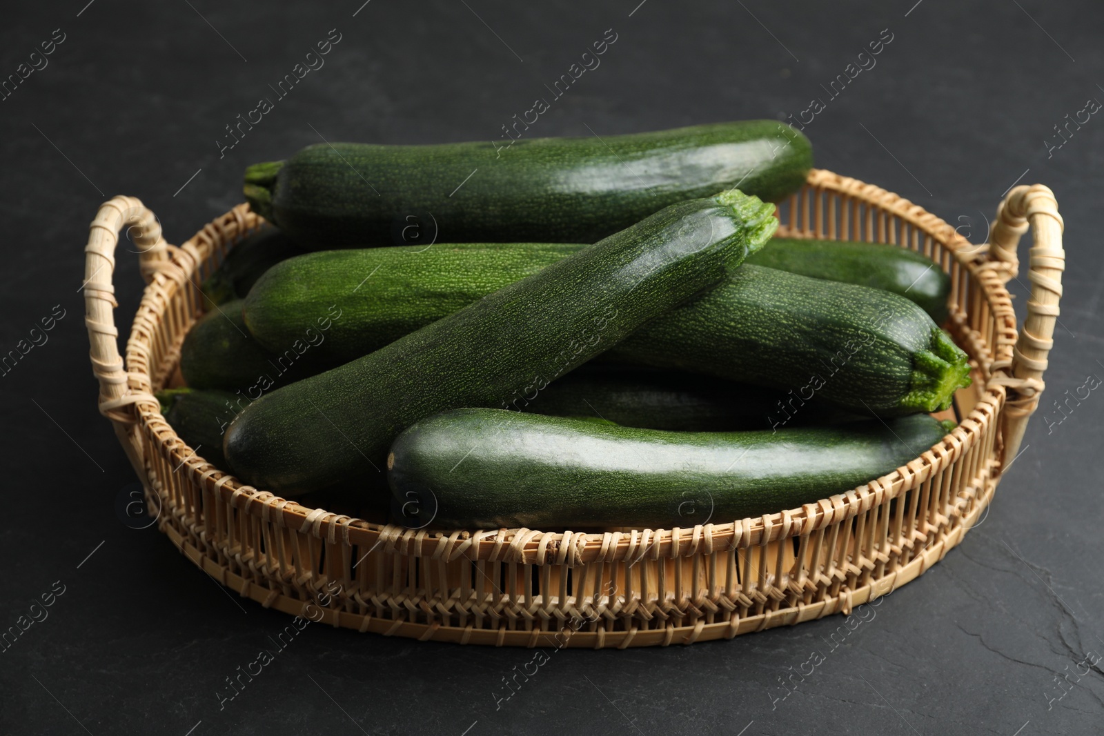 Photo of Basket with green zucchinis on black slate table