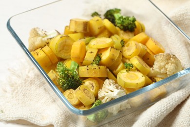 Photo of Baked yellow carrot with broccoli and cauliflowers in glass dish on table, closeup