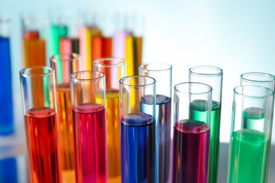 Photo of Many test tubes with colorful liquids on turquoise background, closeup