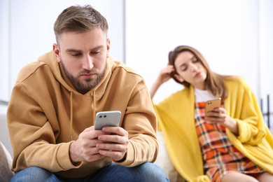 Photo of Couple addicted to smartphones ignoring each other at home. Relationship problems