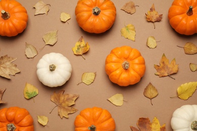 Photo of Different ripe pumpkins and autumn leaves on brown background, flat lay