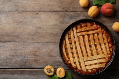 Photo of Delicious apricot pie in baking dish and fresh fruits on wooden table, flat lay. Space for text