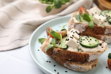 Photo of Tasty vegan sandwiches with tofu, cucumber, tomato and sesame seeds on white tiled table, closeup