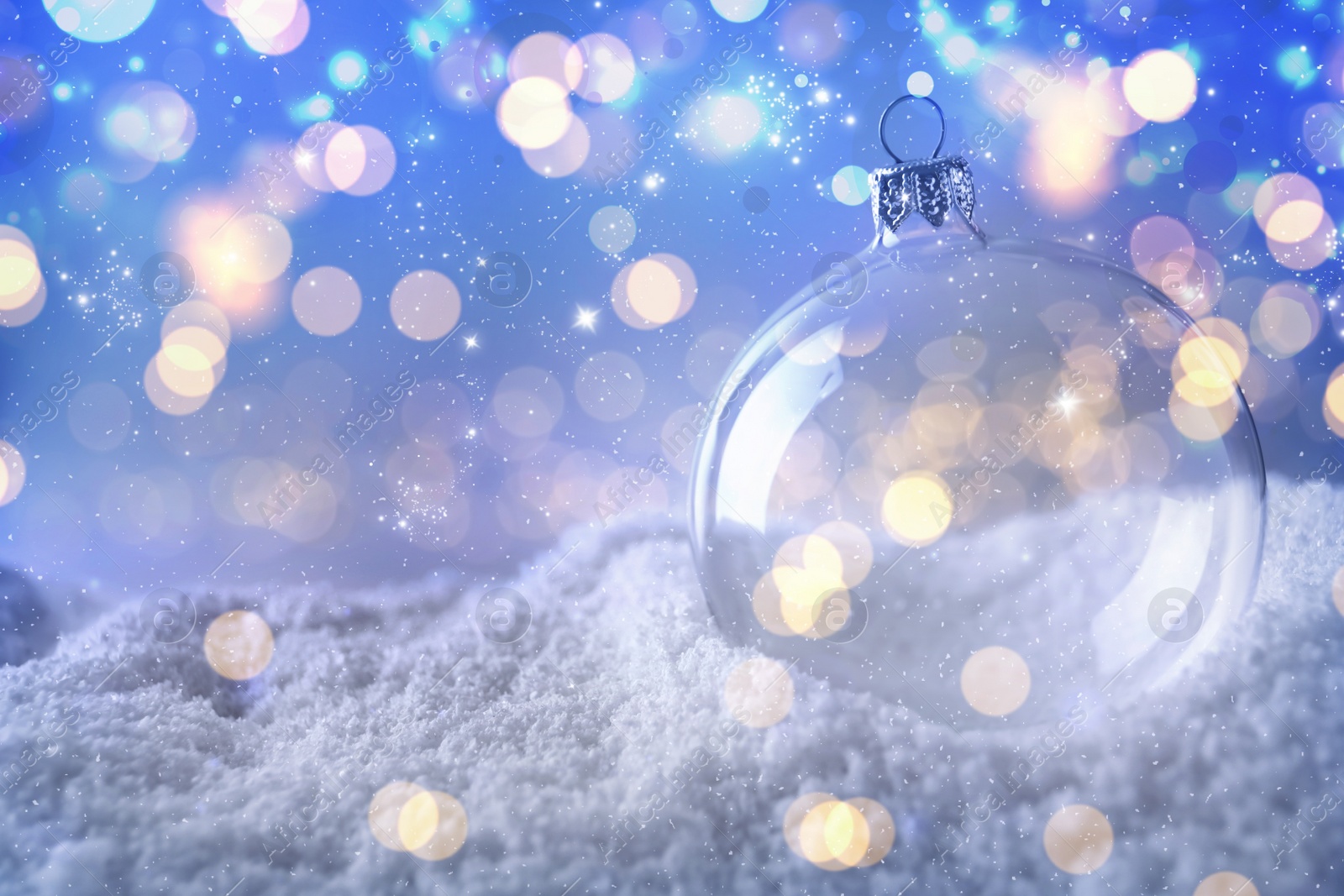 Image of Transparent Christmas ball on snow against blurred fairy lights, space for text. Bokeh effect