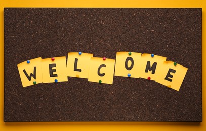 Photo of Corkboard with word Welcome made of paper notes on yellow background, top view