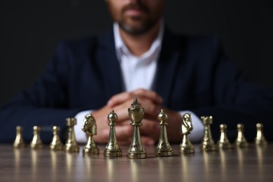 Photo of Man with chess pieces at wooden table against dark background, closeup